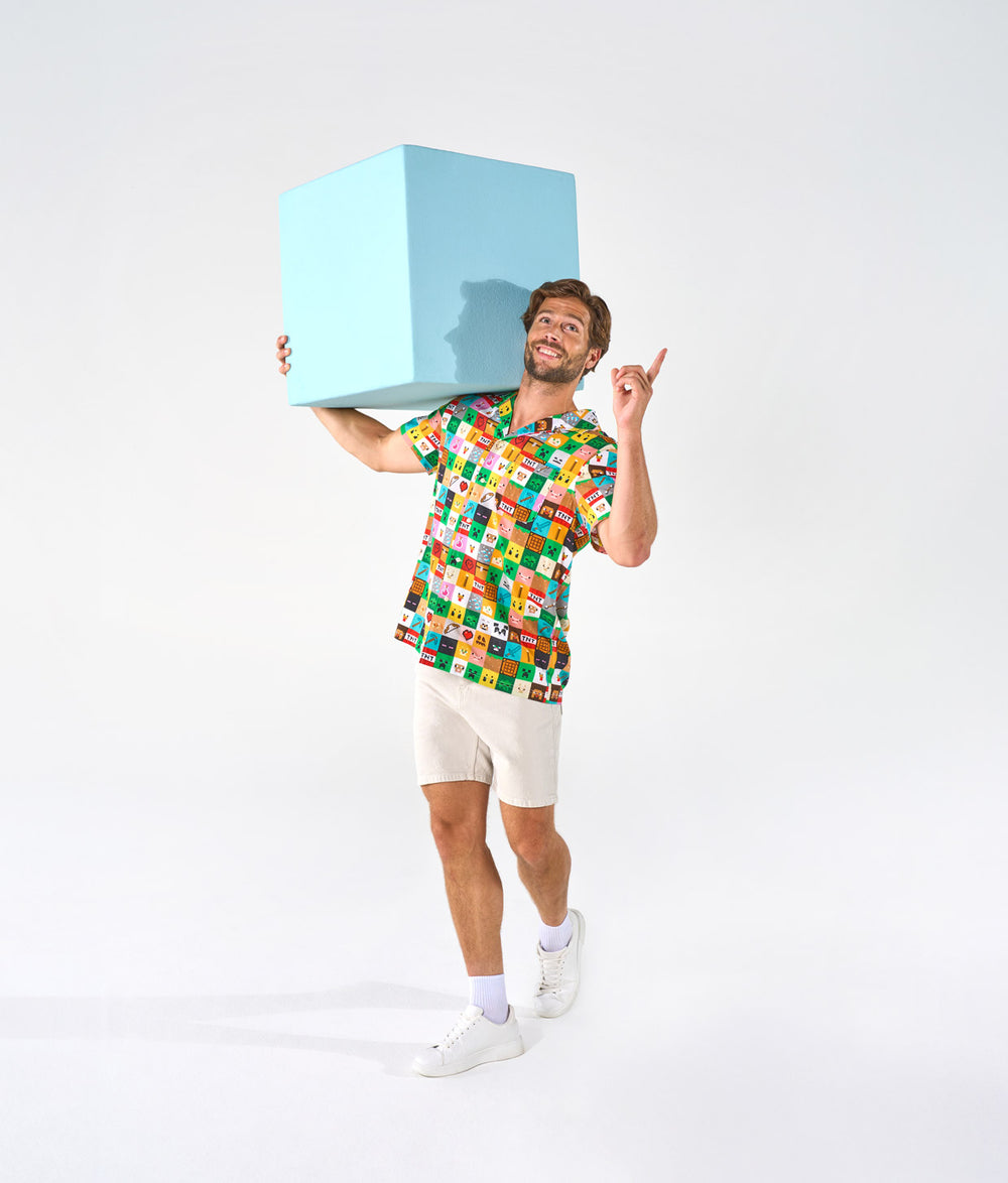 Man wearing a colorful Minecraft shirt holding a light blue cube against a white background