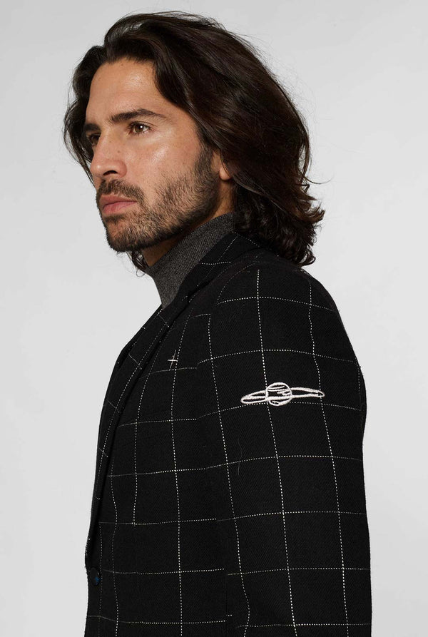 Black casual blazer with white grid pattern worn by man sitting on stool
