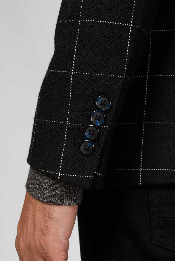 Black casual blazer with white grid pattern worn by man sitting on stool