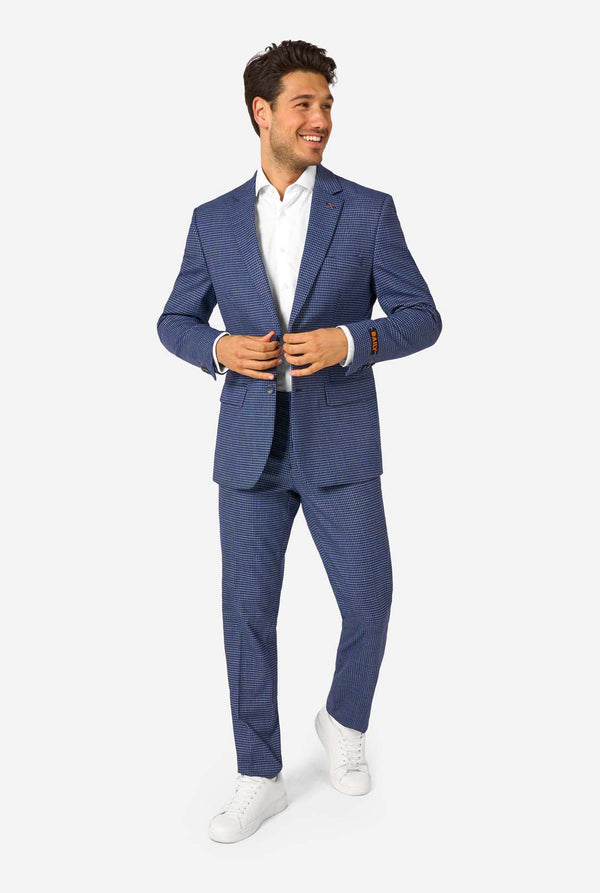 A men wearing a navy and blue checkered suit with a white dress shirt. The suit has a modern fit with two buttons and flap pockets. He stands against a plain white background. Full body image