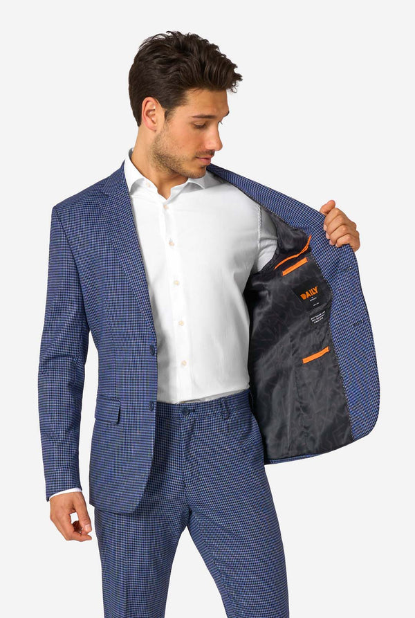 A men wearing a navy and blue checkered suit with a white dress shirt. The suit has a modern fit with two buttons and flap pockets. He stands against a plain white background. Holding his jacket open
