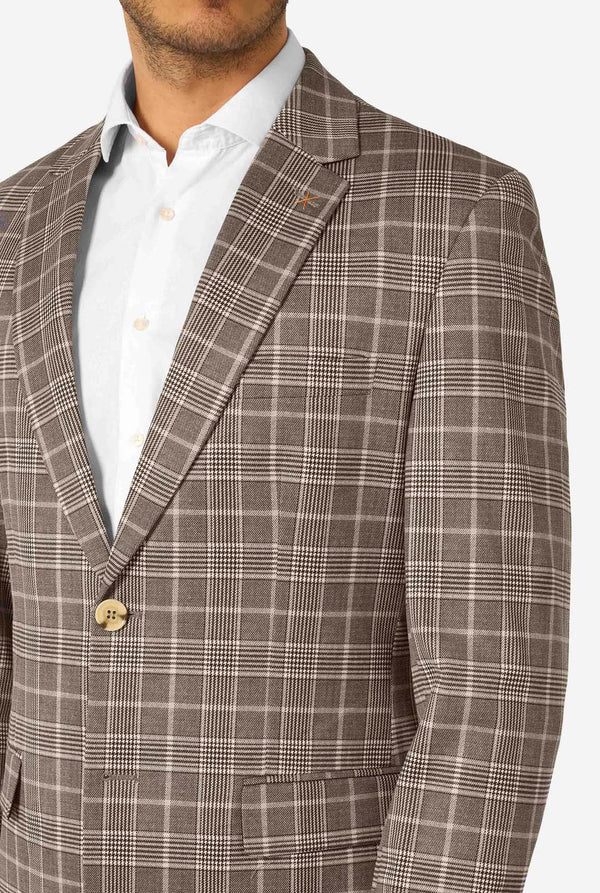 A men wearing a tan checkered suit with a white dress shirt. The suit has a modern fit with two buttons and flap pockets. He stands against a plain white background. Close up of the chest