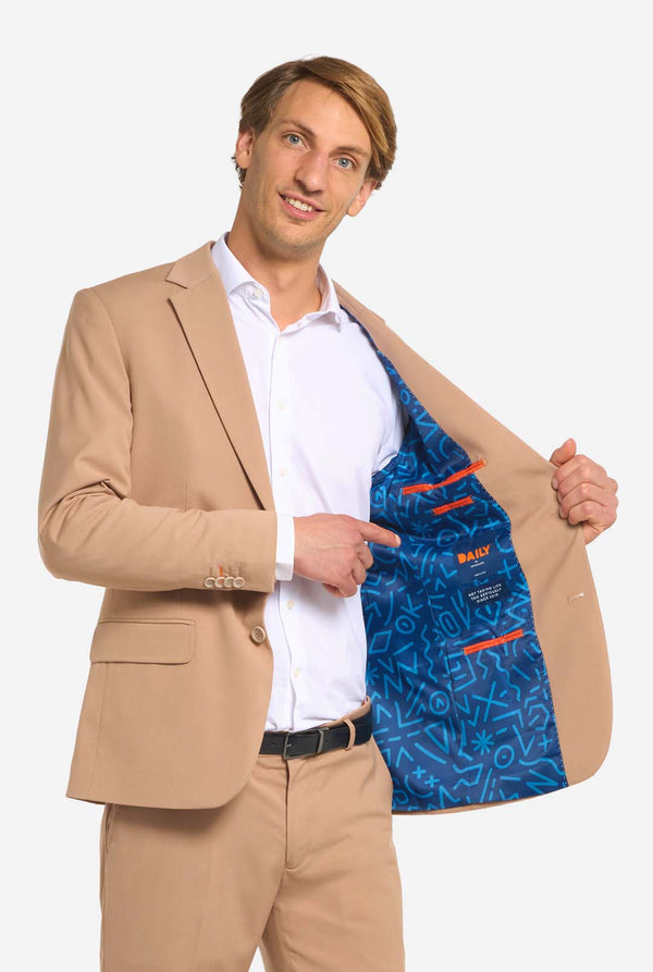 Image with light grey background and man wearing Dark Sand men’s suit and white shirt. Suits consists of blazer and pants. Holding one side of his jacket open.