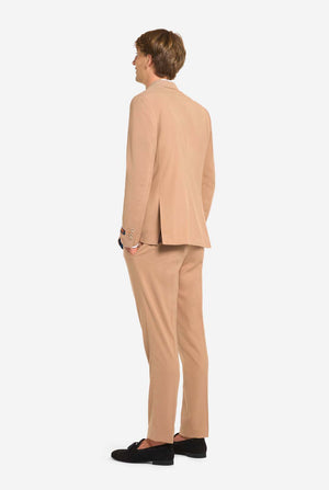 Image with light grey background and man wearing Dark Sand men’s suit and white shirt. Suits consists of blazer and pants. View from the back.