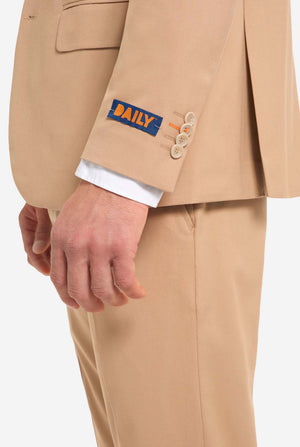 Image with light grey background and man wearing Dark Sand men’s suit and white shirt. Suits consists of blazer and pants. View from the side.