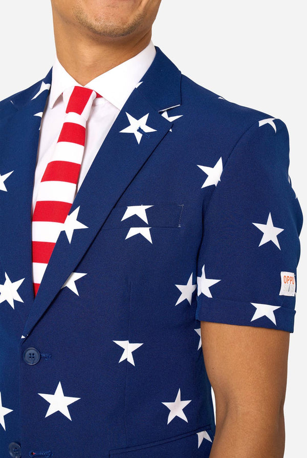 Person wearing a blue blazer with white star patterns, white shirt. Chest close up. 