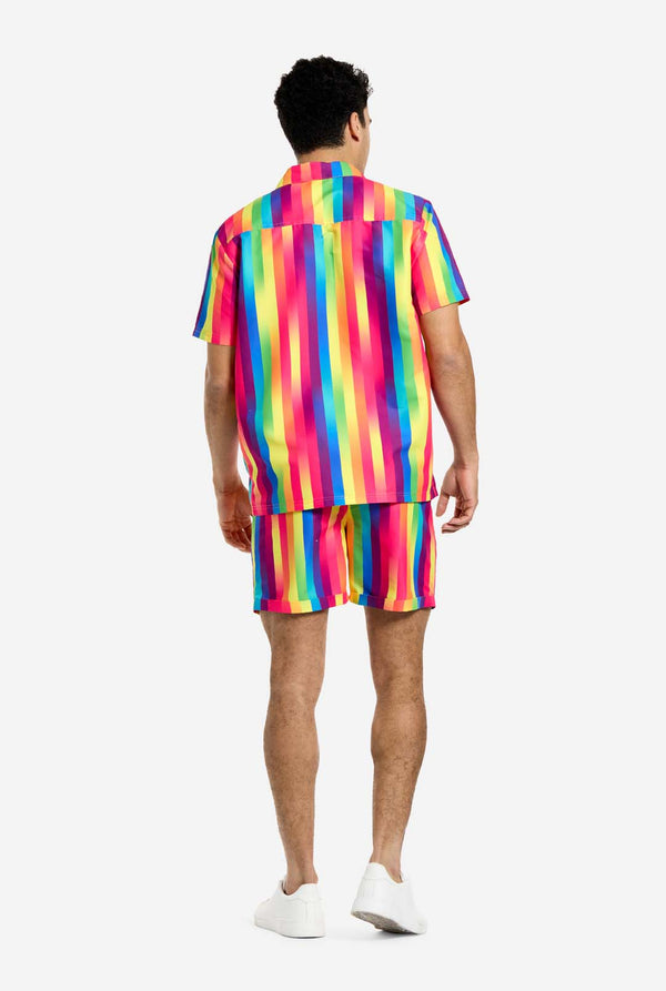 A man is wearing a vertically striped rainbow-colored summer set, consisting of shirt and shorts. He is facing away from the camera and showing the back of the summer set.