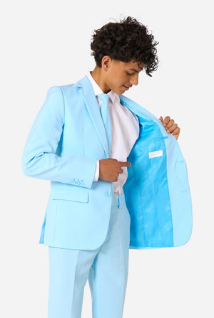 Teen wearing a light blue suit with a white shirt and tie on a light background. Holding one side of the jacket open.