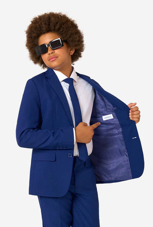 Kid wearing a blue suit with sunglasses, pointing to the jacket pocket on a white background