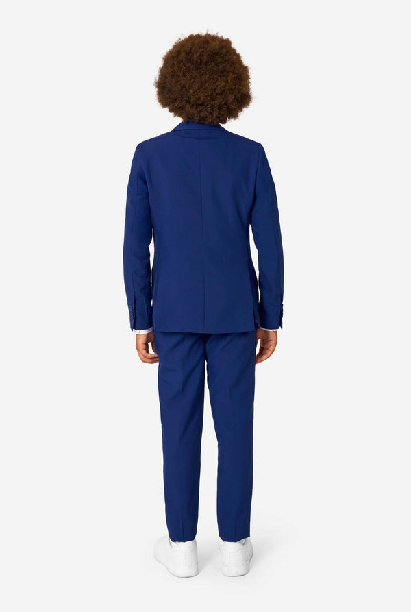 Kid wearing a blue suit standing against a white background, view from the back.