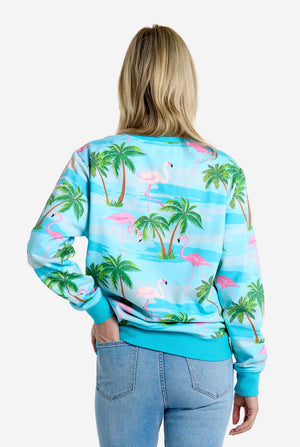 Person wearing a tropical-themed sweatshirt with flamingos and palm trees on a white background