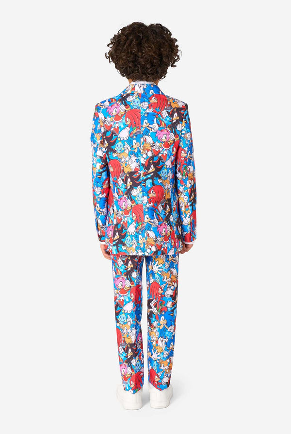 Young boy wearing a vibrant Sonic teen suit featuring colorful prints of Sonic the Hedgehog characters including Sonic, Knuckles, Tails, and Amy, paired with a matching tie and white shirt. View from the back.