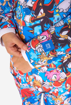 Young boy wearing a vibrant Sonic teen suit featuring colorful prints of Sonic the Hedgehog characters including Sonic, Knuckles, Tails, and Amy, paired with a matching tie and white shirt. Close-up sleeves.