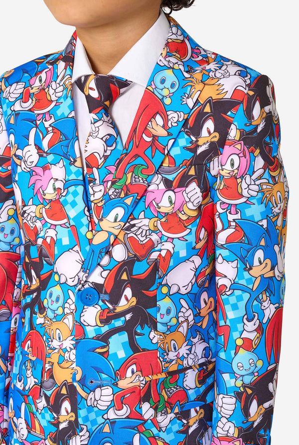 Young boy wearing a vibrant Sonic teen suit featuring colorful prints of Sonic the Hedgehog characters including Sonic, Knuckles, Tails, and Amy, paired with a matching tie and white shirt. Close-up chest.