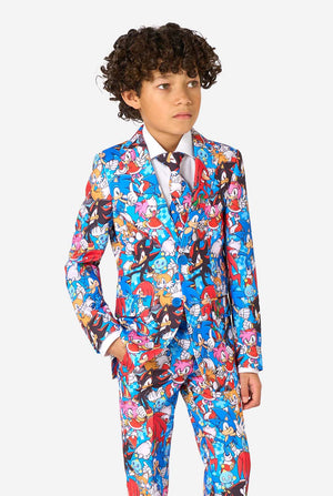 Young boy wearing a vibrant Sonic teen suit featuring colorful prints of Sonic the Hedgehog characters including Sonic, Knuckles, Tails, and Amy, paired with a matching tie and white shirt. Looking to the side.