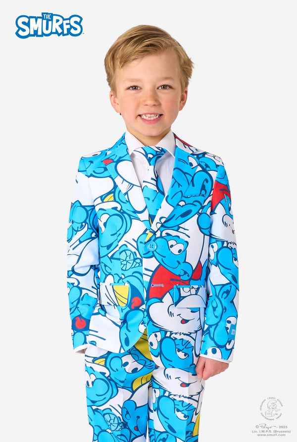 Young boy wearing a colorful Smurfs-themed kids suit featuring vibrant blue cartoon character prints, including jacket, pants, and matching tie, smiling against a plain white background.