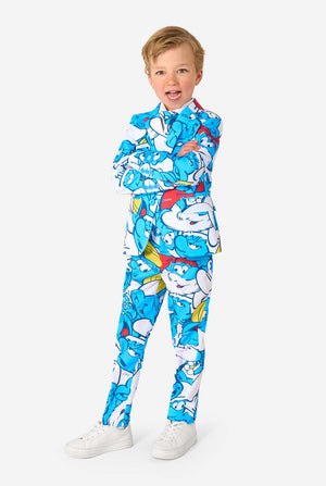 Young boy wearing a colorful Smurfs-themed kids suit featuring vibrant blue cartoon character prints, including jacket, pants, and matching tie, smiling against a plain white background. Full body image.