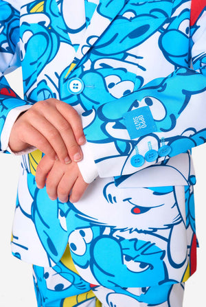Young boy wearing a colorful Smurfs-themed kids suit featuring vibrant blue cartoon character prints, including jacket, pants, and matching tie, smiling against a plain white background. Sleeve close-up.