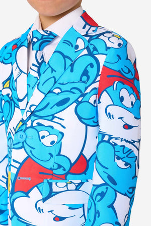 Young boy wearing a colorful Smurfs-themed kids suit featuring vibrant blue cartoon character prints, including jacket, pants, and matching tie, smiling against a plain white background. Chest close-up.