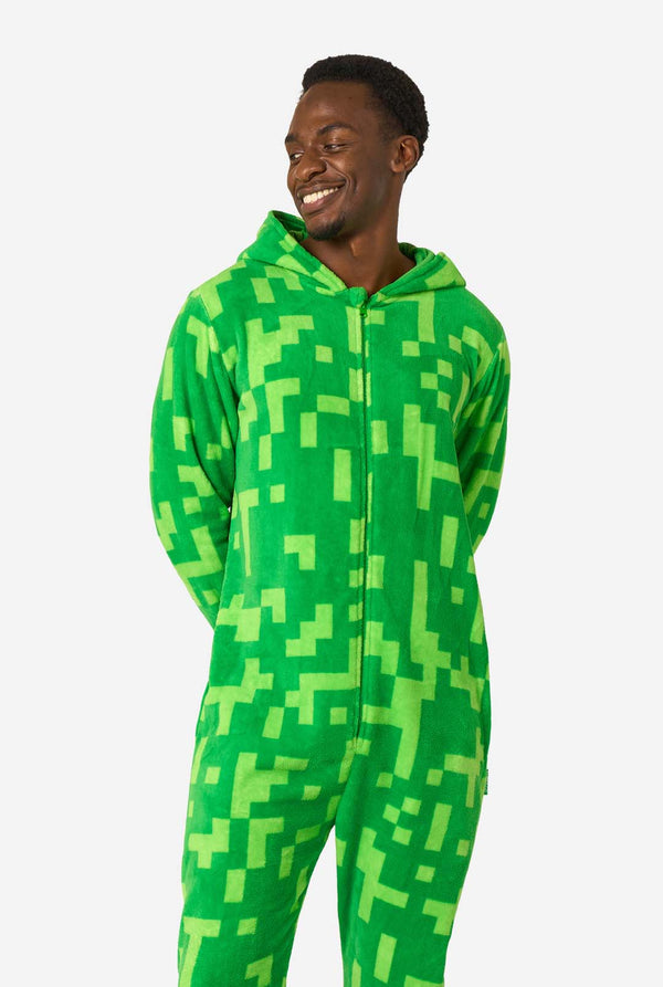 A man wearing green pixelated onesie designed to look like the Minecraft Creeper character. The onesie has a hood with the Creeper’s iconic black pixel face. The man has the hood on his back and is looking to the side.