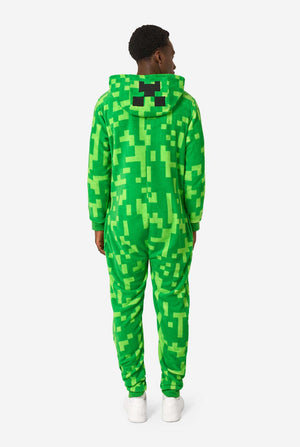 A man wearing green pixelated onesie designed to look like the Minecraft Creeper character. The onesie has a hood with the Creeper’s iconic black pixel face. The man has the hood on his back. View from the back.