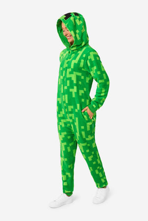 A women wearing green pixelated onesie designed to look like the Minecraft Creeper character. The onesie has a hood with the Creeper’s iconic black pixel face. The women is wearing the hood and is looking down to the ground.