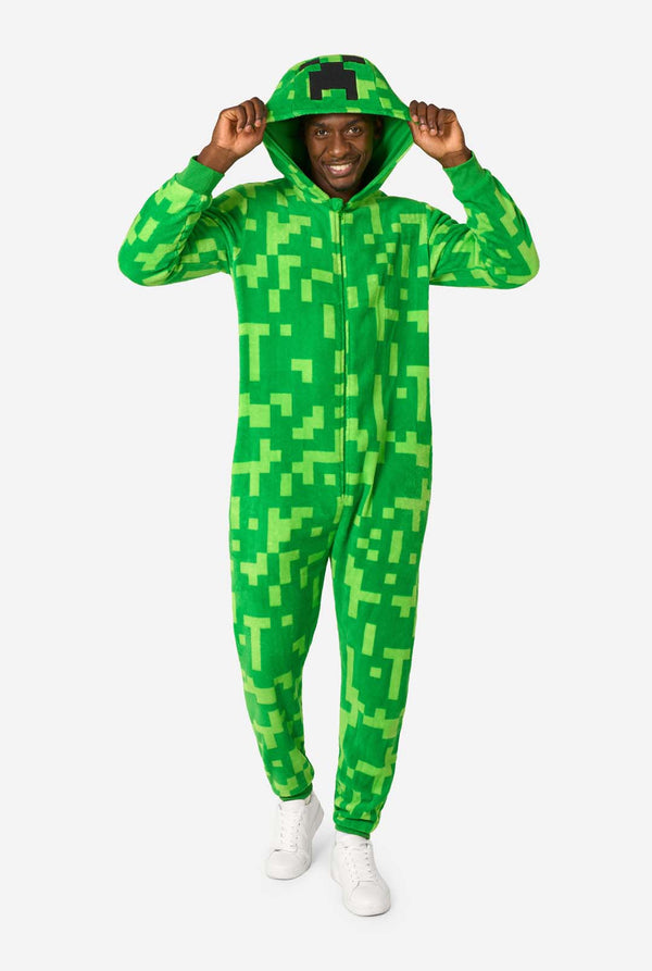 A man wearing green pixelated onesie designed to look like the Minecraft Creeper character. The onesie has a hood with the Creeper’s iconic black pixel face. The man is wearing the hood and is looking into the camera