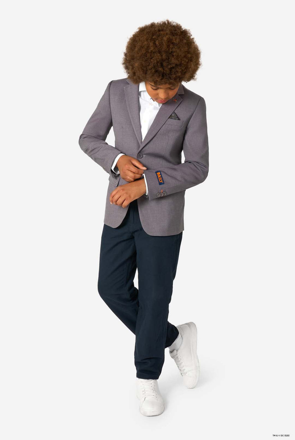 A child smiling while wearing a light grey blazer, white shirt, and dark trousers, looking upward.