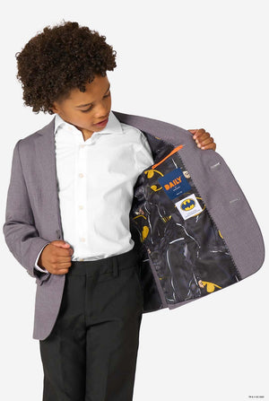 Child wearing a gray blazer with a Batman-themed lining, holding the blazer open to reveal the lining.