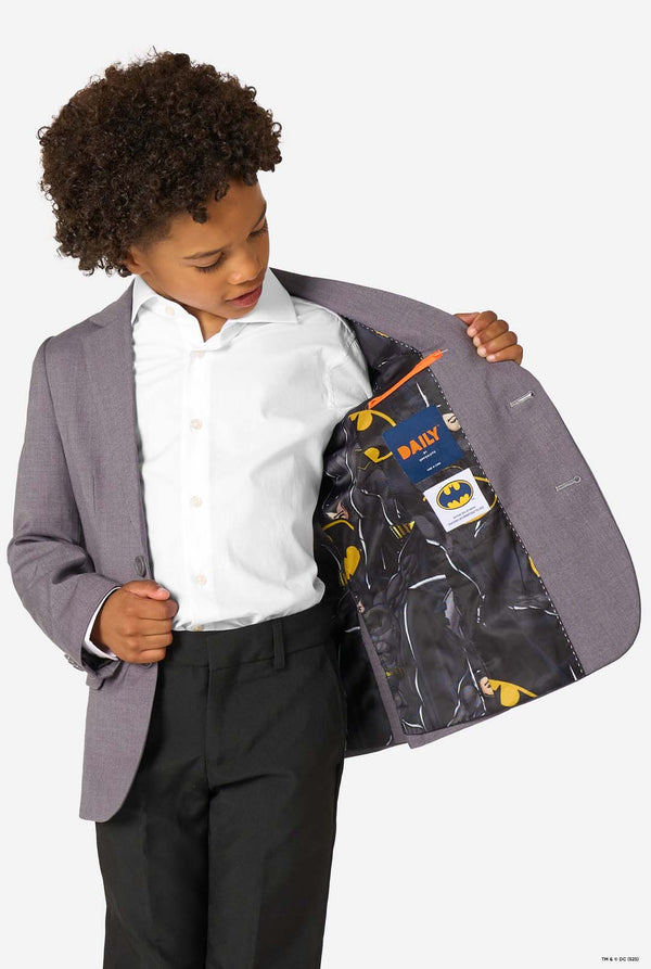 Child wearing a gray blazer with a Batman-themed lining, holding the blazer open to reveal the lining.