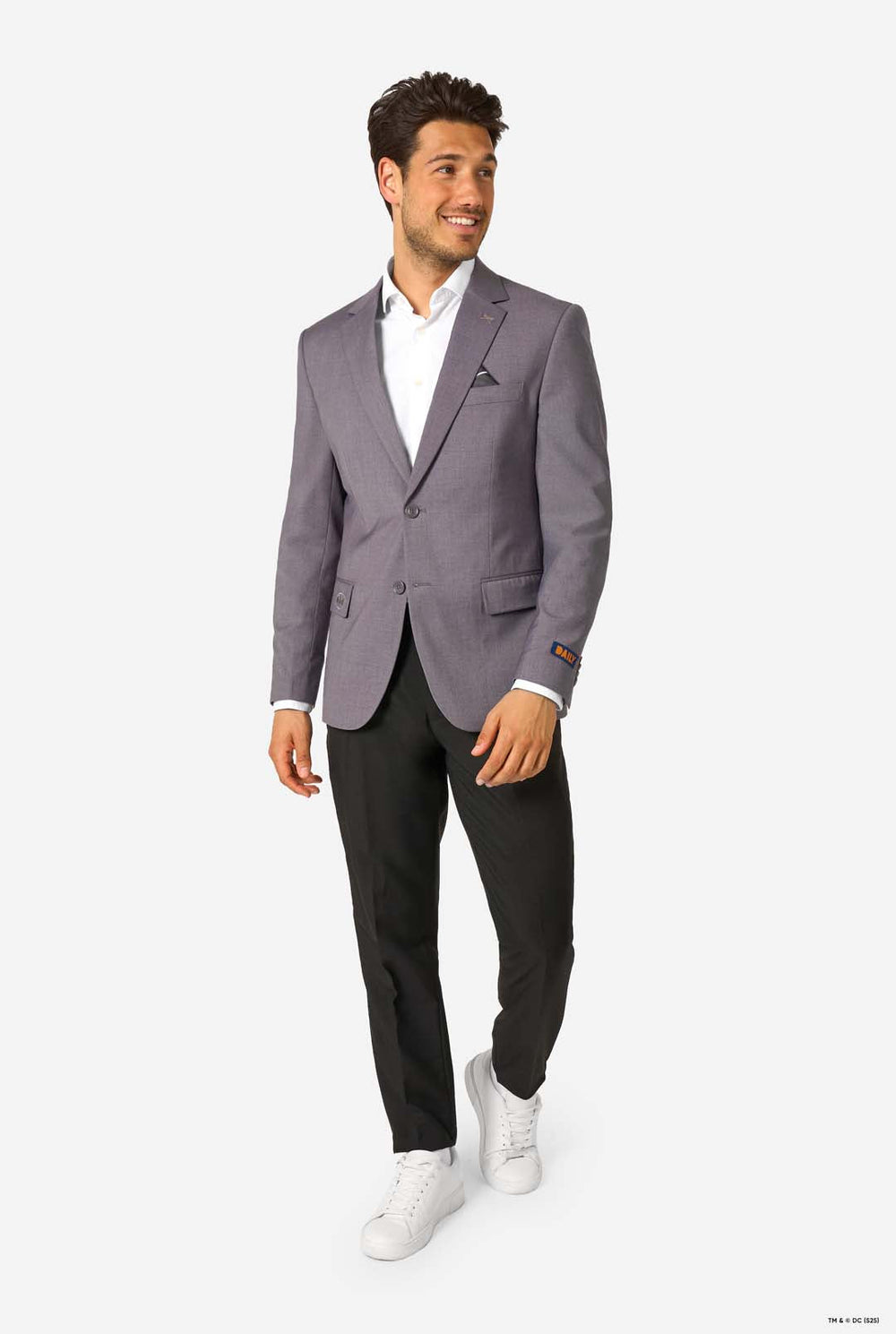 A man wearing a light grey blazer, white shirt, and black trousers, standing and buttoning the jacket.