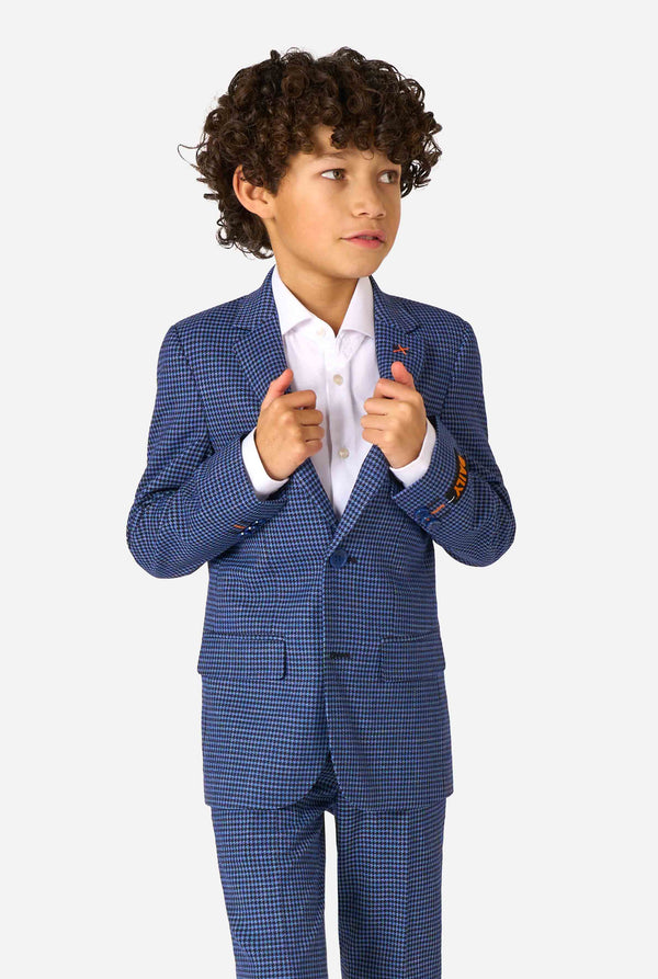 A boy wearing a navy and blue checkered suit with a white dress shirt. The suit has a modern fit with two buttons and flap pockets. He stands against a plain white background.