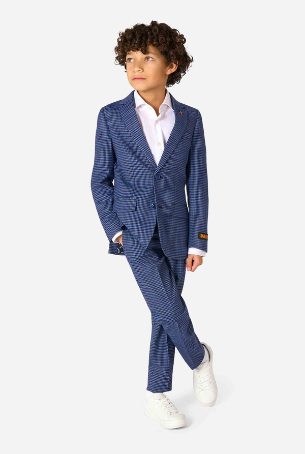 A boy wearing a navy and blue checkered suit with a white dress shirt. The suit has a modern fit with two buttons and flap pockets. He stands against a plain white background. Full body image.