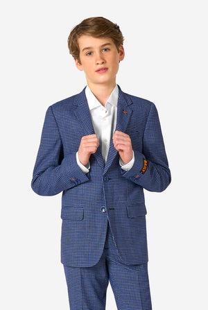 A young boy stands smiling while wearing a formal navy plaid suit jacket over a white button-down shirt. The suit features a subtle check pattern.