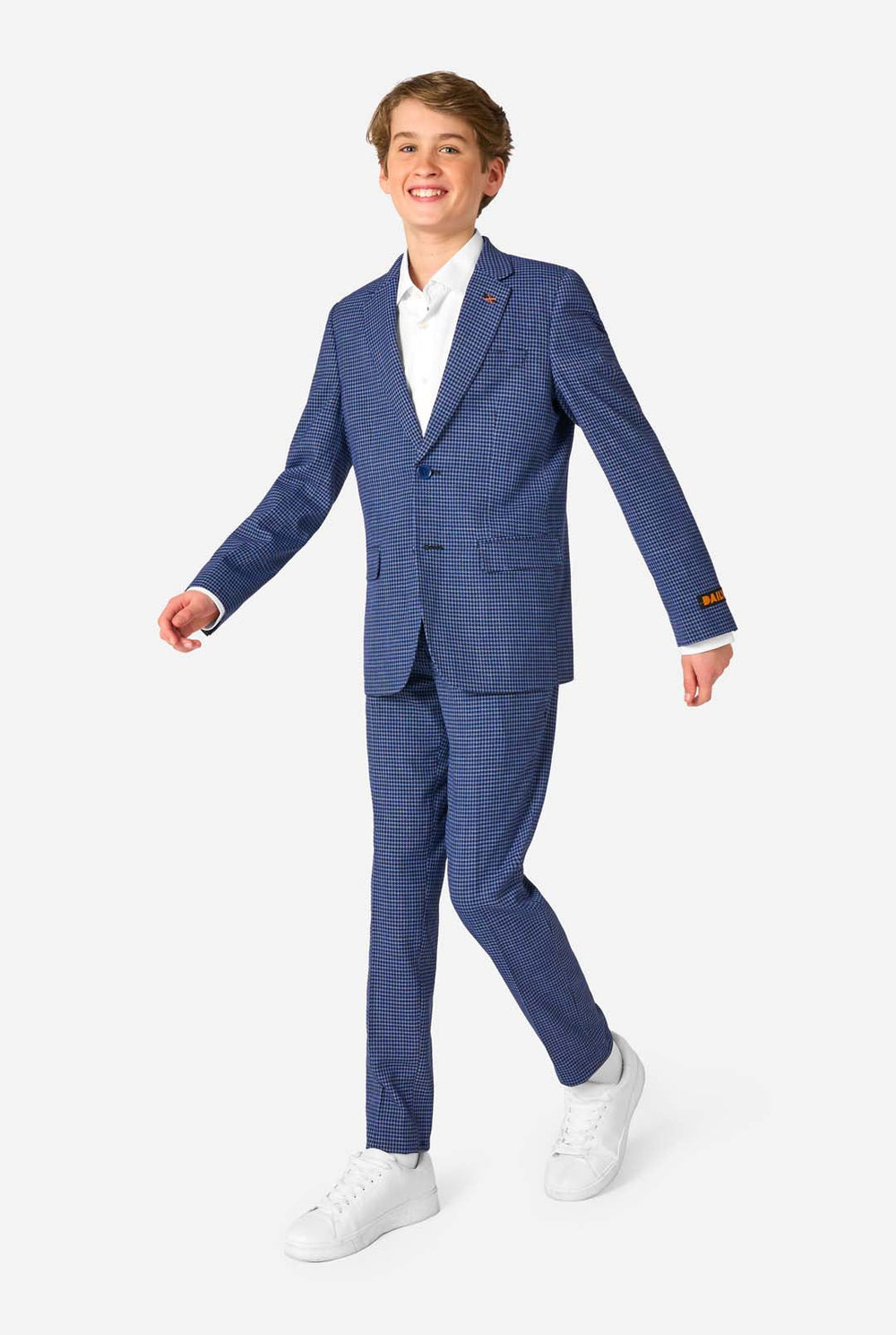 A young boy stands smiling while wearing a formal navy plaid suit jacket over a white button-down shirt. The suit features a subtle check pattern.