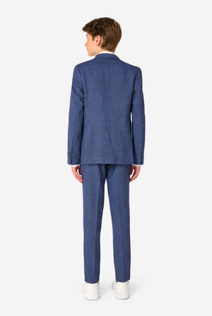 A young boy stands smiling while wearing a formal navy plaid suit jacket over a white button-down shirt. The suit features a subtle check pattern. View from the back