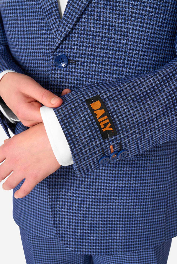 A young boy stands smiling while wearing a formal navy plaid suit jacket over a white button-down shirt. The suit features a subtle check pattern. Close up of the sleeves