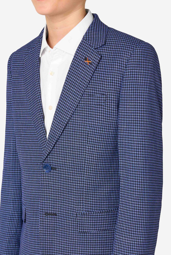 A young boy stands smiling while wearing a formal navy plaid suit jacket over a white button-down shirt. The suit features a subtle check pattern. Close up of the chest