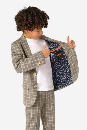 A boy wearing a tan checkered suit with a white dress shirt. The suit has a modern fit with two buttons and flap pockets. He stands against a plain white background. Holding one side of the jacket open.