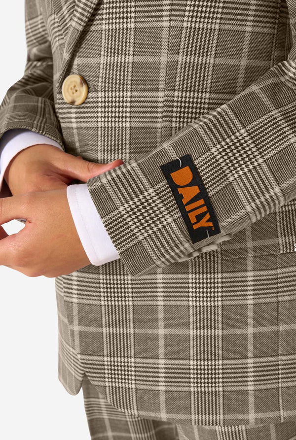 A boy wearing a tan checkered suit with a white dress shirt. The suit has a modern fit with two buttons and flap pockets. He stands against a plain white background. Close up of the sleeves.