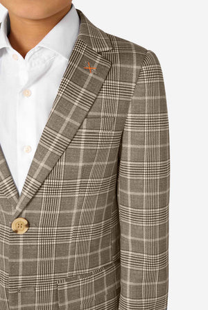 A boy wearing a tan checkered suit with a white dress shirt. The suit has a modern fit with two buttons and flap pockets. He stands against a plain white background. Close up of the chest.
