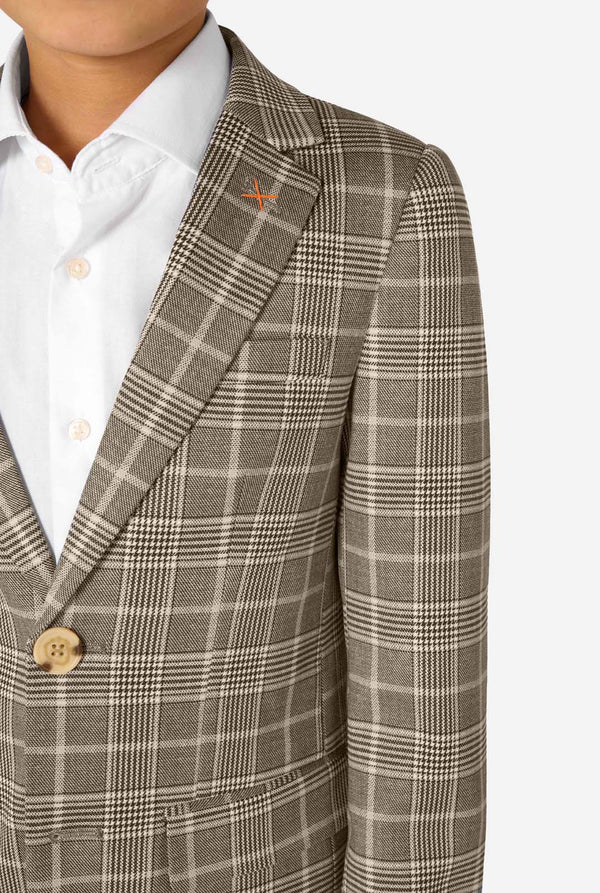 A boy wearing a tan checkered suit with a white dress shirt. The suit has a modern fit with two buttons and flap pockets. He stands against a plain white background. Close up of the chest.