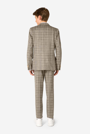 A young boy stands smiling while wearing a formal tan and beige plaid suit jacket over a white button-down shirt. The suit features a subtle check pattern. View from the back