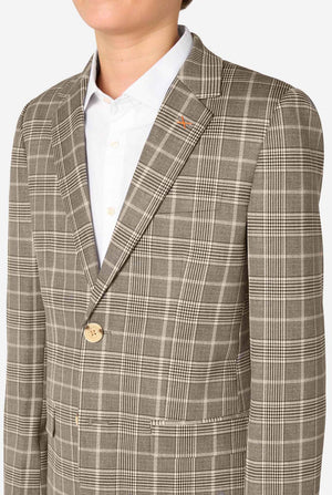 A young boy stands smiling while wearing a formal tan and beige plaid suit jacket over a white button-down shirt. The suit features a subtle check pattern. Close up of the chest
