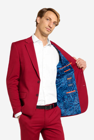 Image with light grey background and man wearing Bright Burgundy men’s suit and white shirt. Suits consists of blazer and pants. Holding one side of his jacket open.