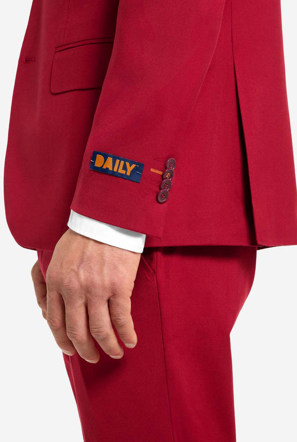 Image with light grey background and man wearing Bright Burgundy men’s suit and white shirt. Suits consists of blazer and pants. View from the side.