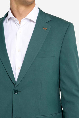 Image with light grey background and man wearing dark green men’s suit and white shirt. Suits consists of blazer and pants. Chest close up.