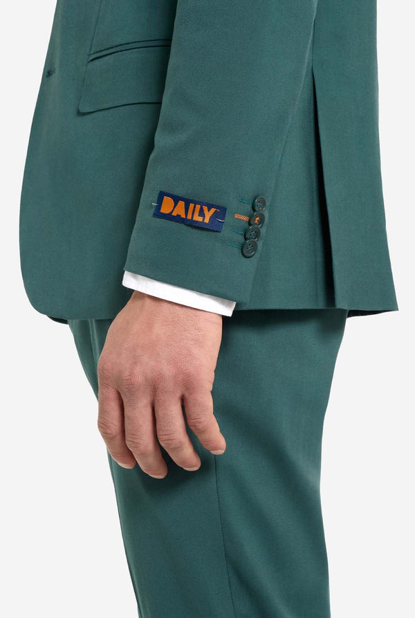 mage with light grey background and man wearing dark green men’s suit and white shirt. Suits consists of blazer and pants. Side view and showing bottom part of the pants and lower part of the blazer.