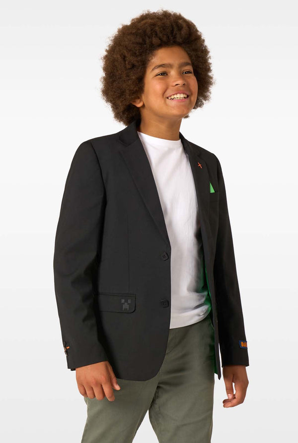 Child wearing a black blazer over a white shirt with a green graphic, standing against a plain background.