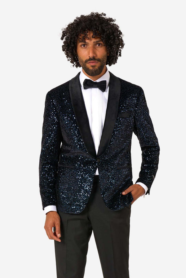 A man poses in a navy sequined blazer or dinner jacket, wearing a solid white shirt underneath.